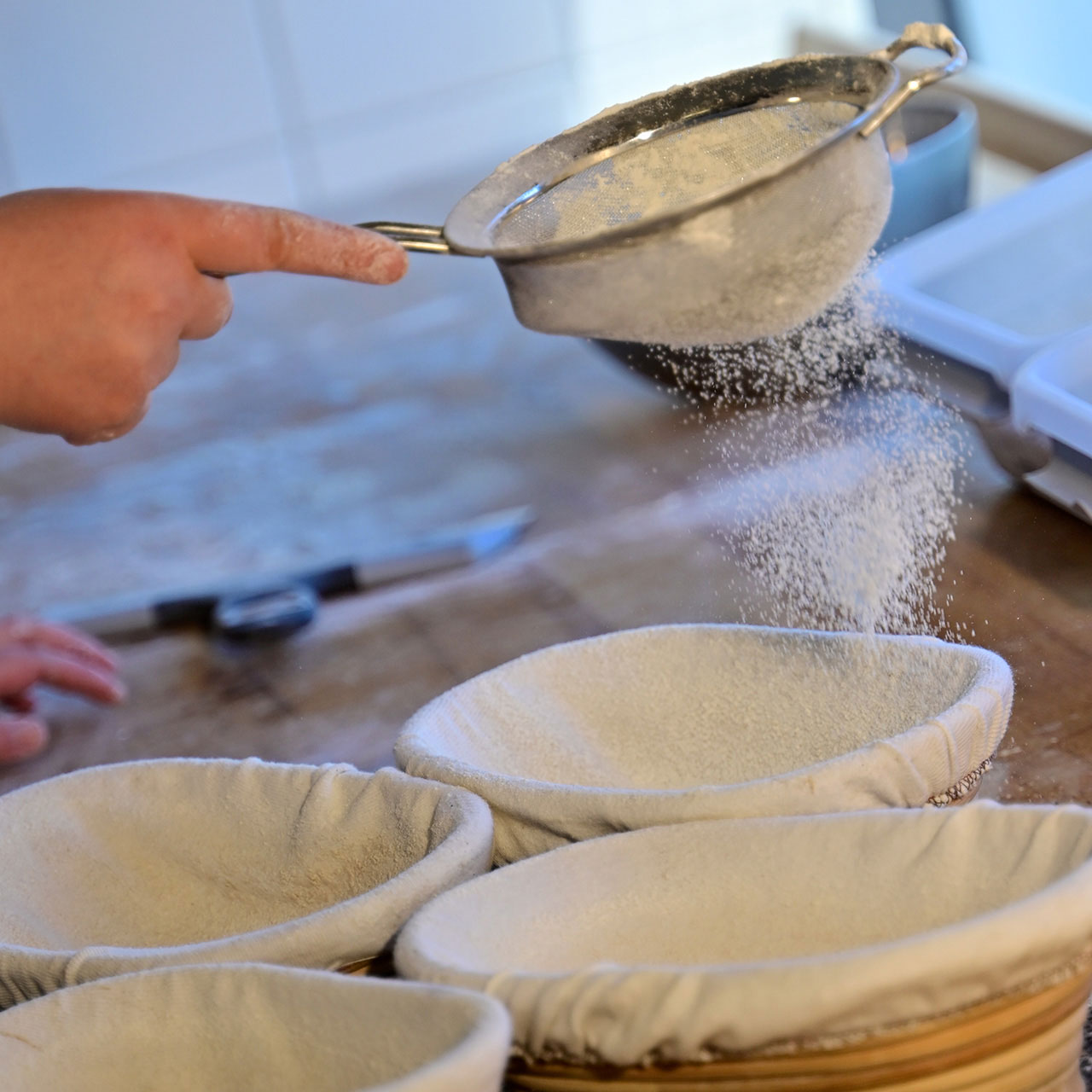 En sil skakas ovanför brödformar. Mjöl faller ner och täcker formen från silen.
